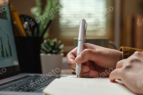 Preview: close uop woman hand writing on notebook at worknig desk at home