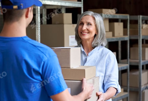 Preview: Happy mature female manager giving parcels boxes to courier in warehouse.