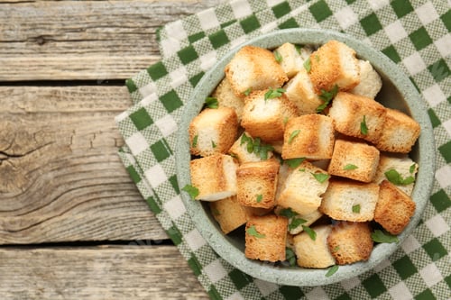 Preview: Tasty crispy croutons with cut parsley in bowl on wooden table, top view. Space for text