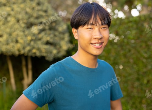 Preview: Smiling teenage asian boy with braces standing outdoors in casual clothing