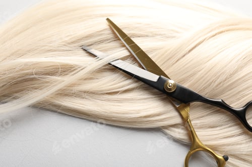 Preview: Blonde hair lock and scissors on light grey background, above view