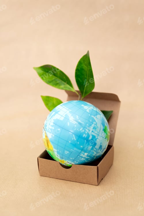 Preview: Earth Globe in Cardboard Box with Green Leaves on Beige Background, Sustainable Packaging Concept