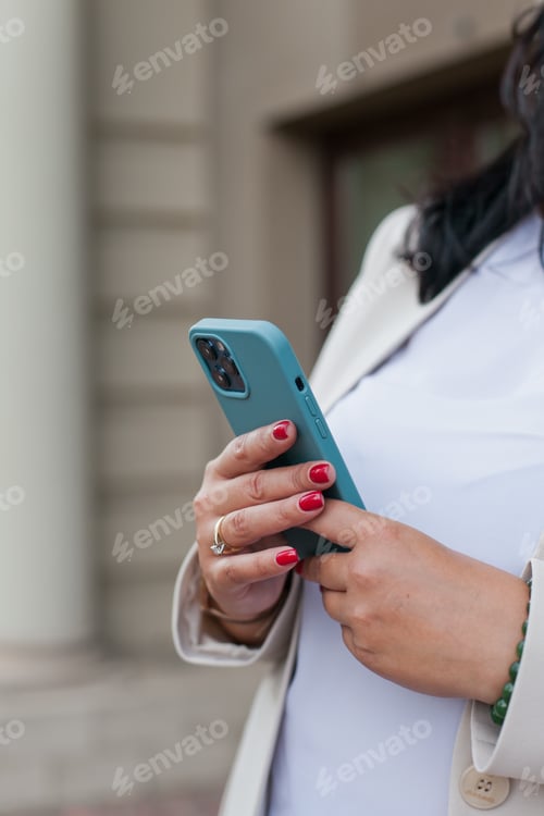 Preview: Businesswoman in white jacket holding using social media, or texting standing near office building