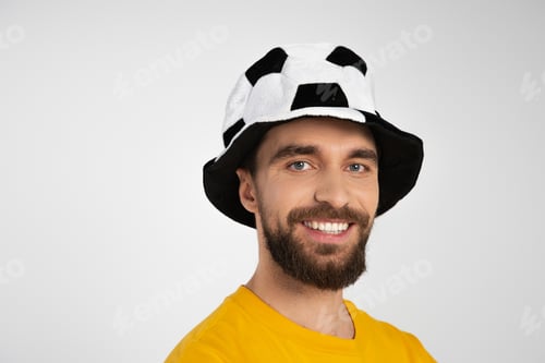 Preview: portrait of bearded man in football fan hat smiling at camera isolated on grey