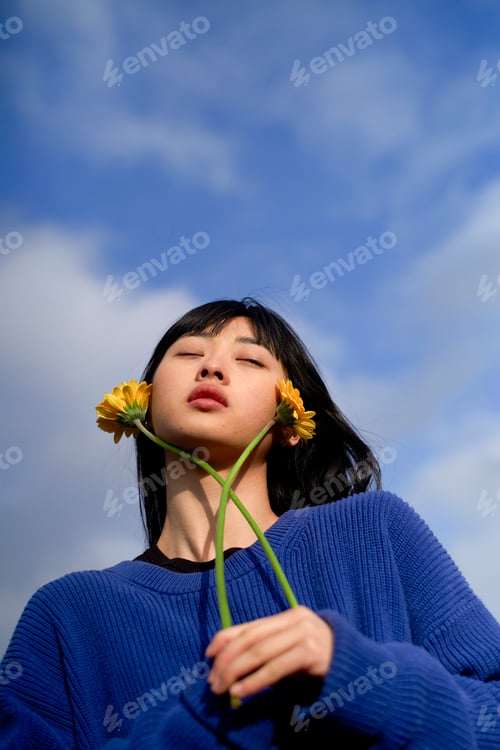 Preview: Woman in blue sweater holding flowers against a clear, blue sky. Brandenburg, Germany