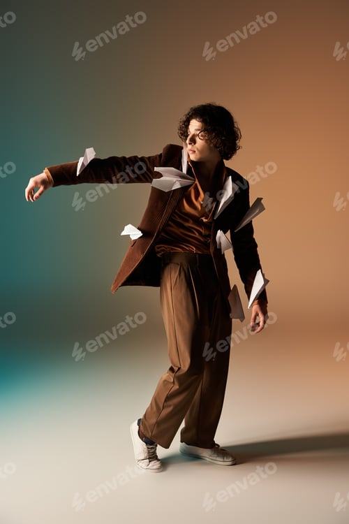 Preview: Curly-haired young man in stylish corduroy blazer playfully poses with paper planes
