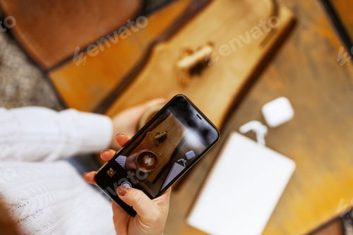 Preview: Woman hands taking a picture of a coffee cup with smart phone and laptop at a coffee shop.