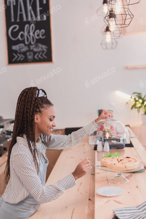 Preview: Smiling african american barista taking a piece of pie from glass cake stand