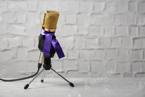 Preview: Microphone with purple awareness ribbon on table against white wall, space for text