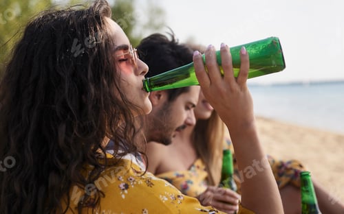 Preview: Close up of girl drinking beer with friends on the beach.