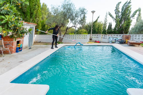 Preview: Woman preparing and cleaning the pool for the swimming area with water vacuum cleaner in the hands