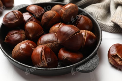 Preview: Fresh edible sweet chestnuts in frying pan on white tiled table, closeup