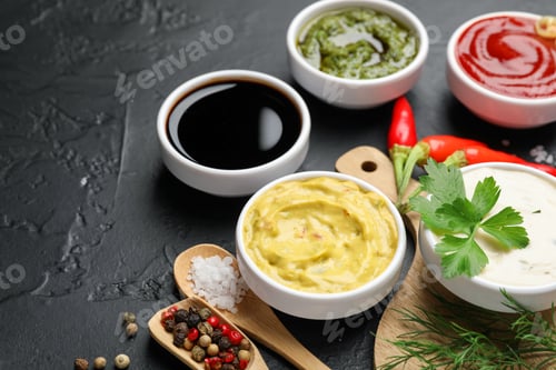 Preview: Different sauces, spices and herbs on black table, closeup