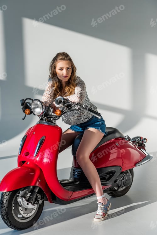 Preview: stylish woman in shorts sitting on red scooter