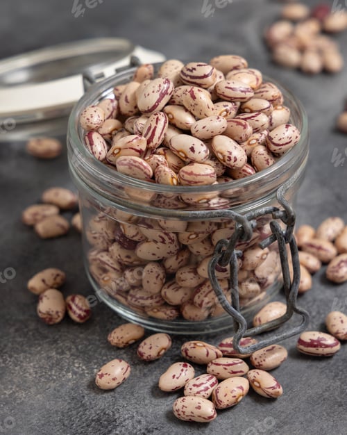 Preview: Glass jar full of dried pinto beans on gray closeup. Traditional Latin American legumes