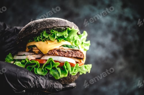 Preview: Hands in black gloves hold a big black burger with marble beef patty, cheese and fresh vegetables