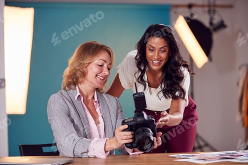 Preview: Mature Female Fashion Photographer With Client Looking At Images From Shoot On Camera In Studio