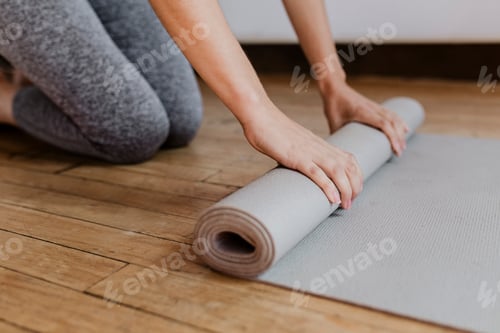 Preview: Woman Rolling Exercise Mat on Wooden Floor