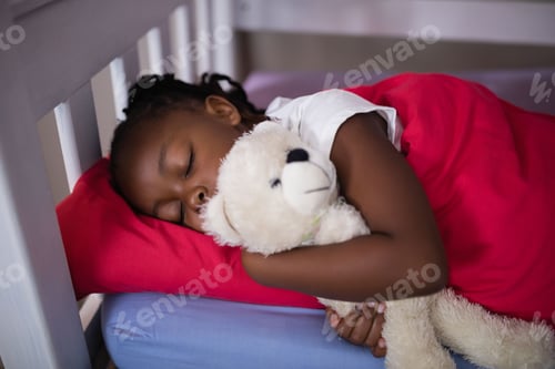 Preview: African American child sleeping in bedroom on bed frame hugging white teddy bear under red blanket