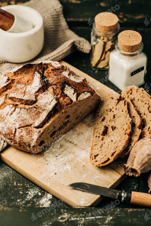 Preview: Vertical shot of a loaf and slices of fresh bread on a wooden board in a kitchen