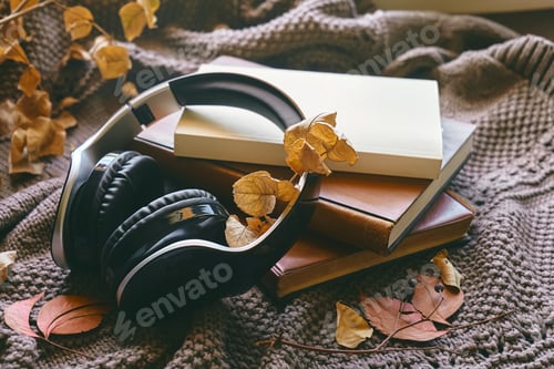 Preview: Audiobook or podcast in fall season. Wireless headphones, books and autumn leaves on knitted plaid