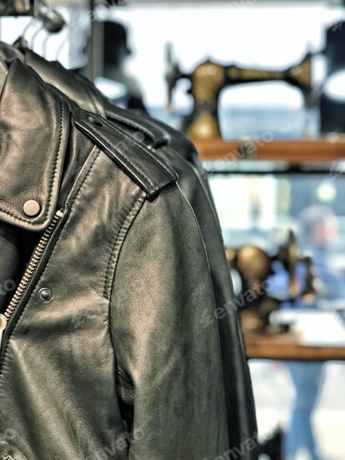 Preview: Black leather jacket with vintage sewing machines on display in storefront background