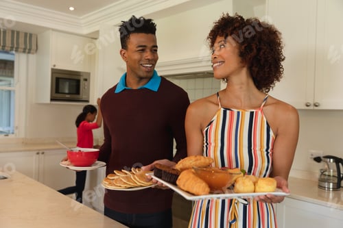Preview: Happy african american couple preparing food in kitchen for breakfast for family and smiling
