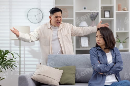 Preview: Man yelling in frustration at calm woman sitting on grey couch at home