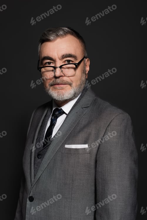 Preview: senior businessman in formal wear and eyeglasses looking at camera isolated on dark grey