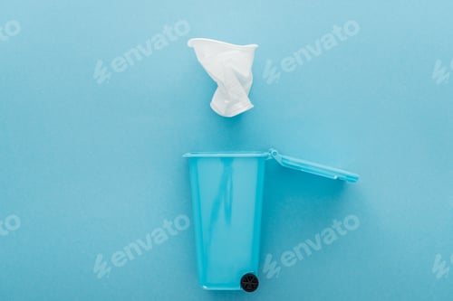 Preview: top view of white crumpled plastic cup falling down toy trash can on blue background