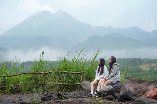 Preview: Two Young Asian Women Sitting Peacefully on Rocks with Misty Mountain View in the Background