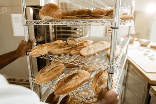 Preview: cropped shot of baker driving shelves of fresh bread on baking manufacture