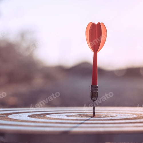 Preview: Close up red dart arrow hitting target centre dartboard on sunset background.