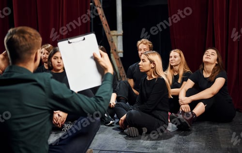 Preview: Sitting on the floor. Group of actors in dark colored clothes on rehearsal in the theater