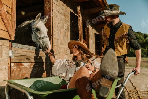 Preview: Young cowboy is driving a cowgirl in wheelbarrow and she is petting horse