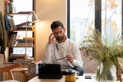 Preview: Young male is feeling exhausted after using laptop in room. Guy looking at screen with tired face
