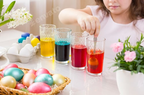 Preview: Cute little girl painting Easter eggs in glasses with liquid dye.