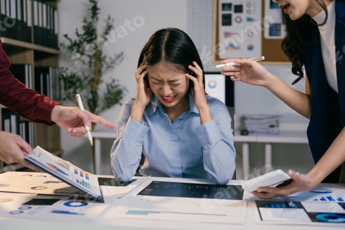 Preview: Stressed businesswoman having headache and covering ears with hands while colleagues blaming her for