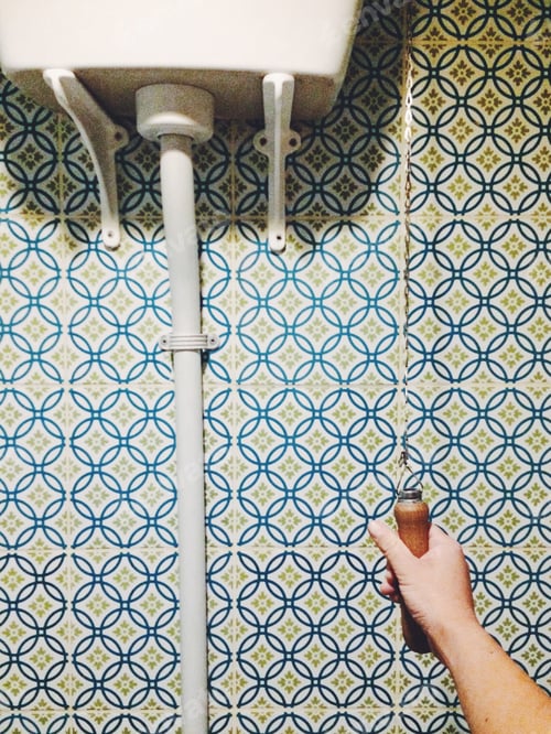 Preview: Hand holding a vintage toilet flush against colorful tiles
