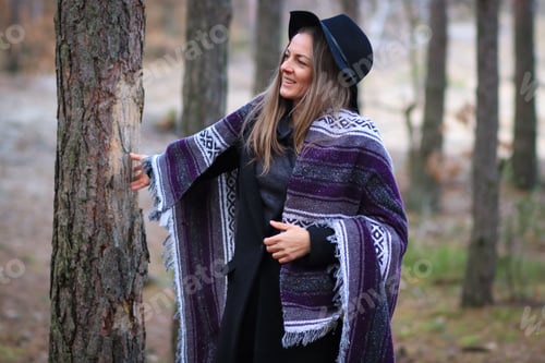 Preview: Photo a young woman wearing a hat and wrapped in blanket on forest path.Millennial life.