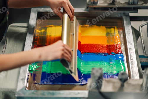 Preview: Close up of graphic worker's hands screen printing with squeegee.