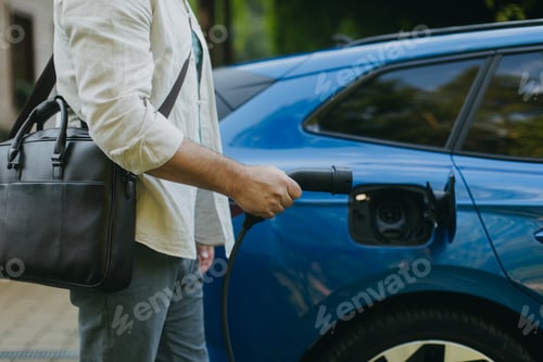 Preview: Close up of businessman charging his electric car in front of house. Pluging charger in charging