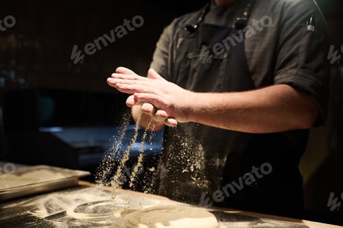 Preview: Hands of young chef rubbing flour between palms and sprinkling it on dough