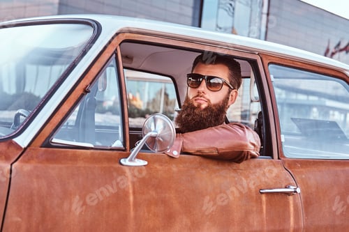 Preview: Bearded male in sunglasses dressed in brown leather jacket driving a retro car.