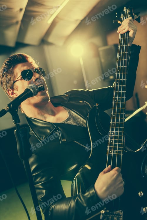 Preview: good-looking guitarist in sunglasses singing song in microphone while playing electic guitar