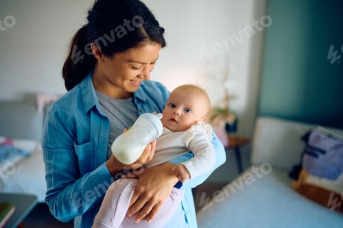Preview: Happy mother feeding her infant with baby formula at home.