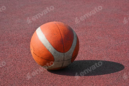 Preview: Orange basketball ball on red outdoors court