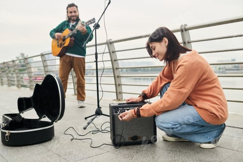 Preview: Young Caucasian Woman Adjusting Amplifier While Young Man Playing Guitar Outdoors