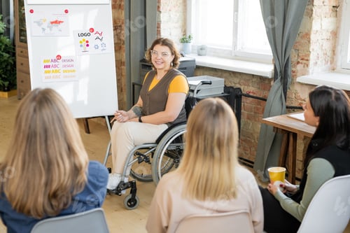 Preview: Group of young female designers sitting on chairs in row in front of colleague