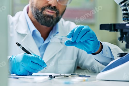 Preview: Close up of microbiologist taking notes while examining sample on microscope slide.